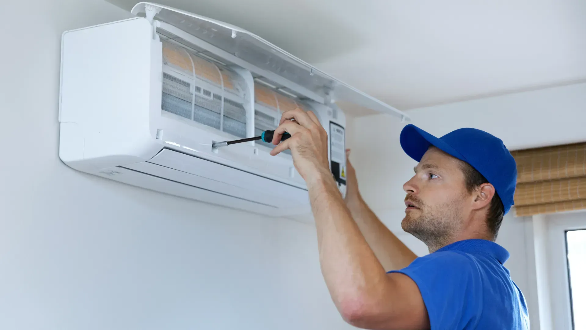 A man is fixing an air conditioner with a screwdriver.