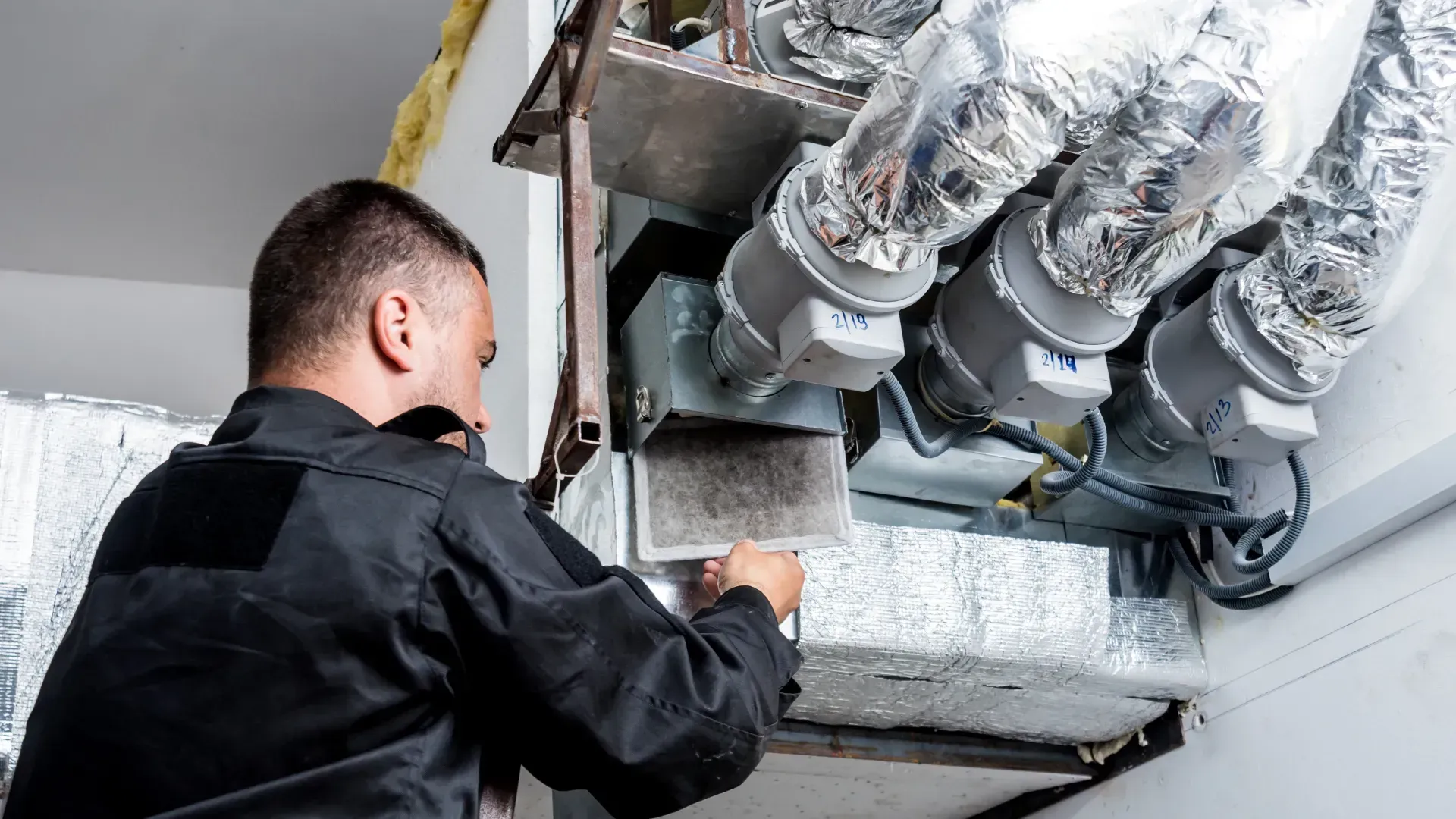 A man is working on a ventilation system in a building.