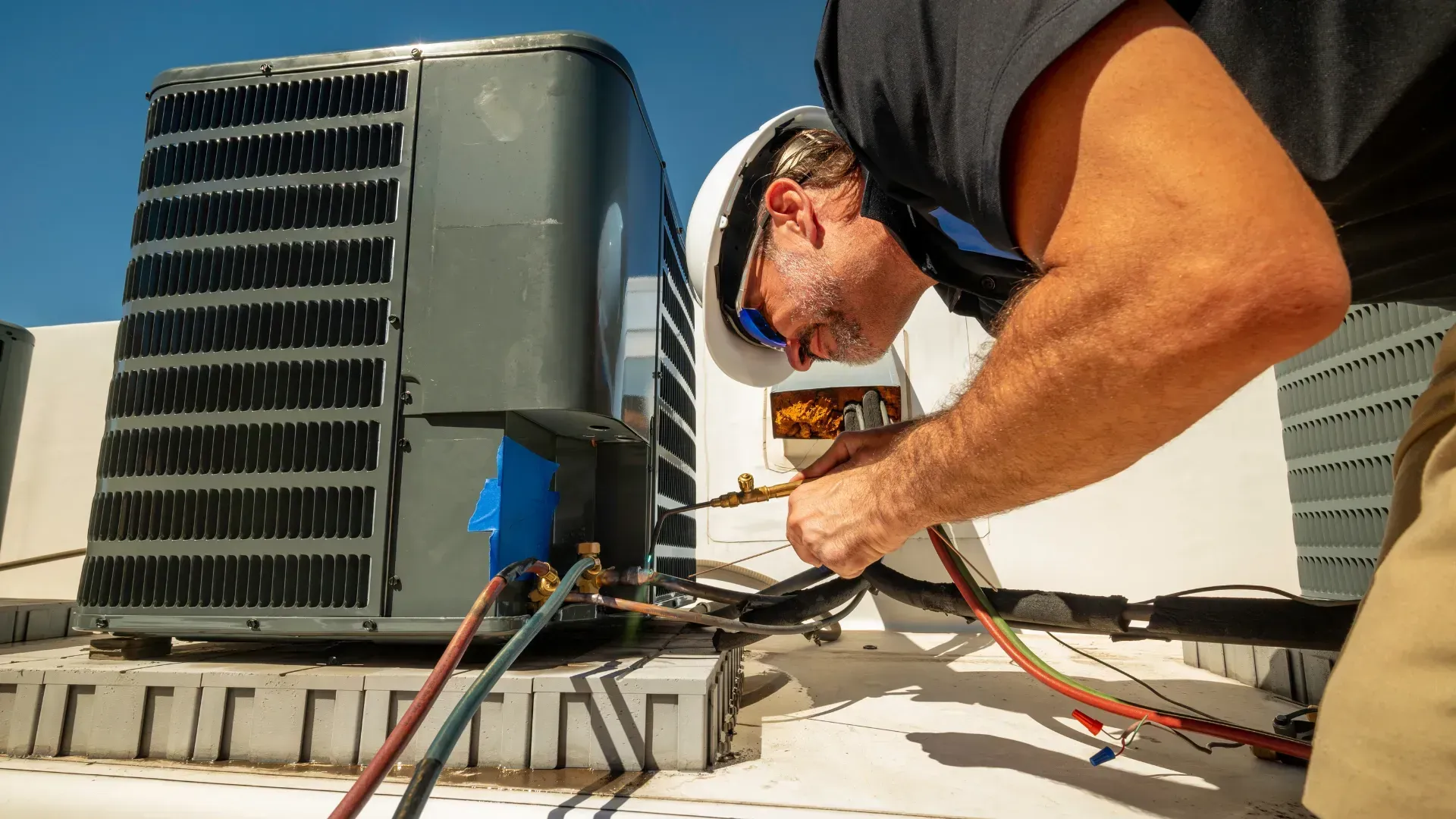 A man is working on an air conditioner on the roof of a building.