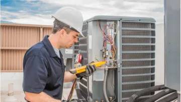 A man wearing a hard hat is working on an air conditioner.