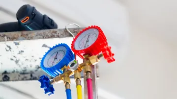 Two pressure gauges are hanging from a ceiling next to a drill.