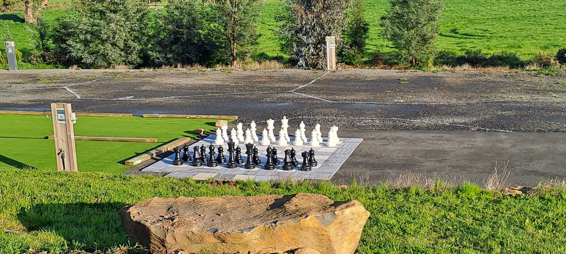 A chess set is sitting on top of a rock on the side of a road.