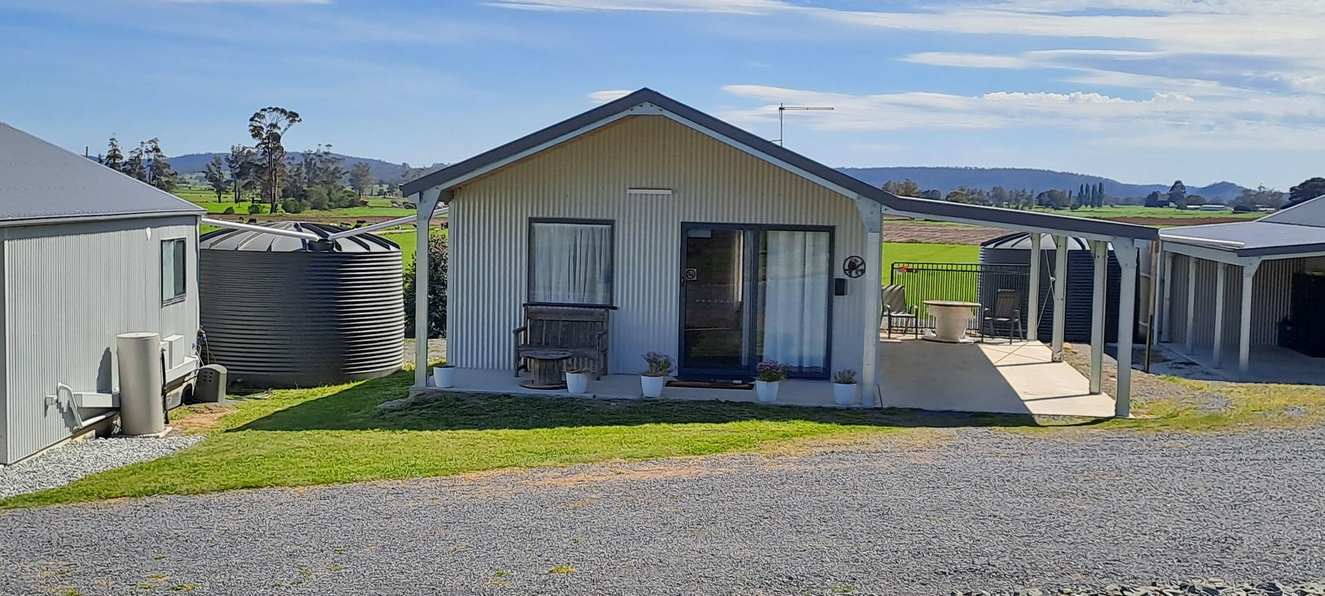 A white house with a black roof is sitting on top of a gravel road.