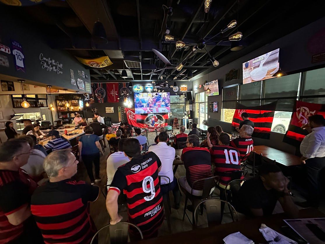 A group of people are sitting at tables in a restaurant watching a soccer game.