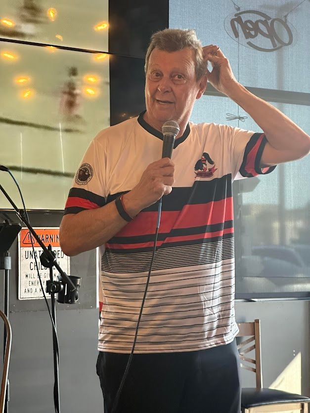 A man in a striped shirt is holding a microphone and adjusting his hair.