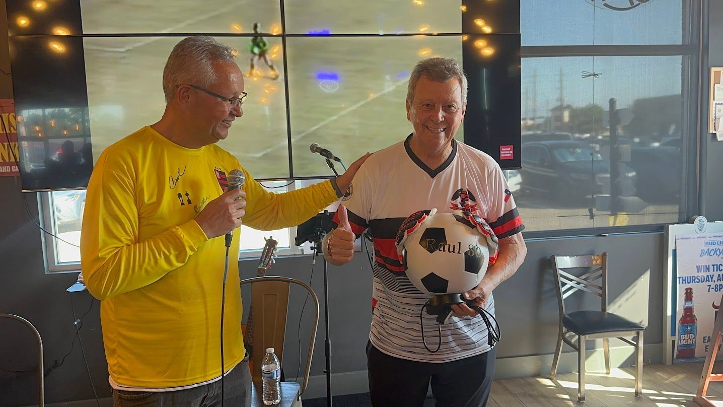 Two men are standing next to each other holding a soccer ball.