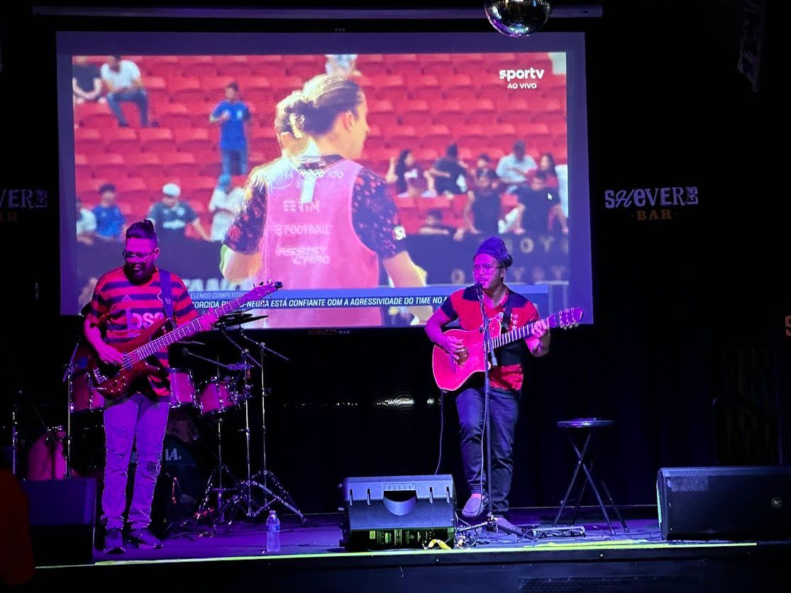 Two men playing guitars on a stage in front of a large screen that says sports
