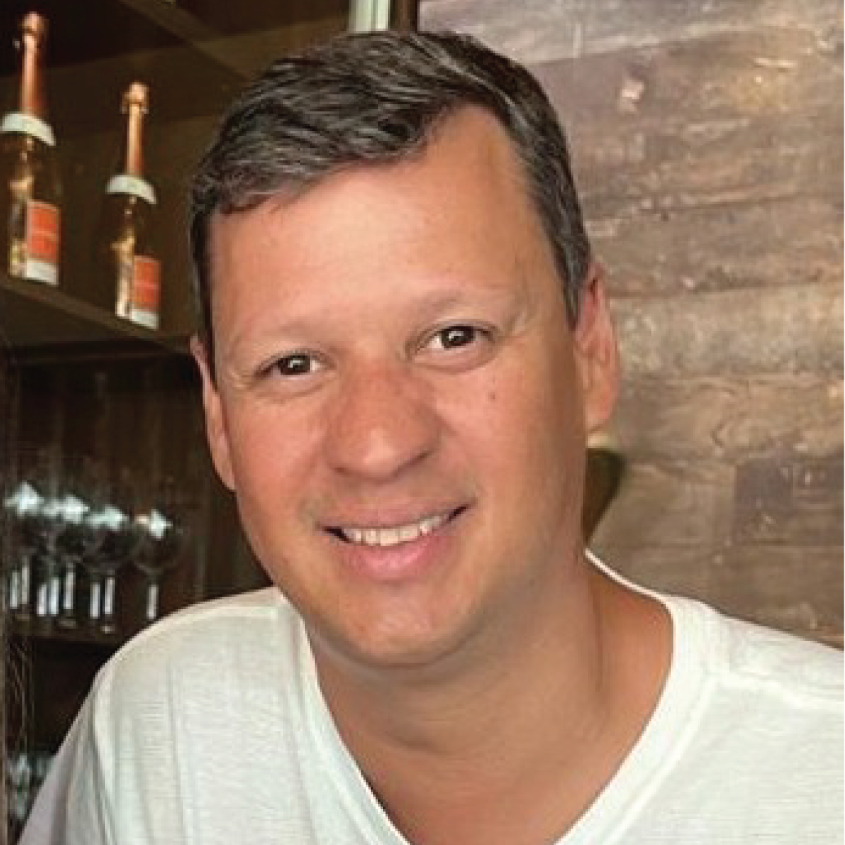 A man in a white shirt is smiling in front of a bar.