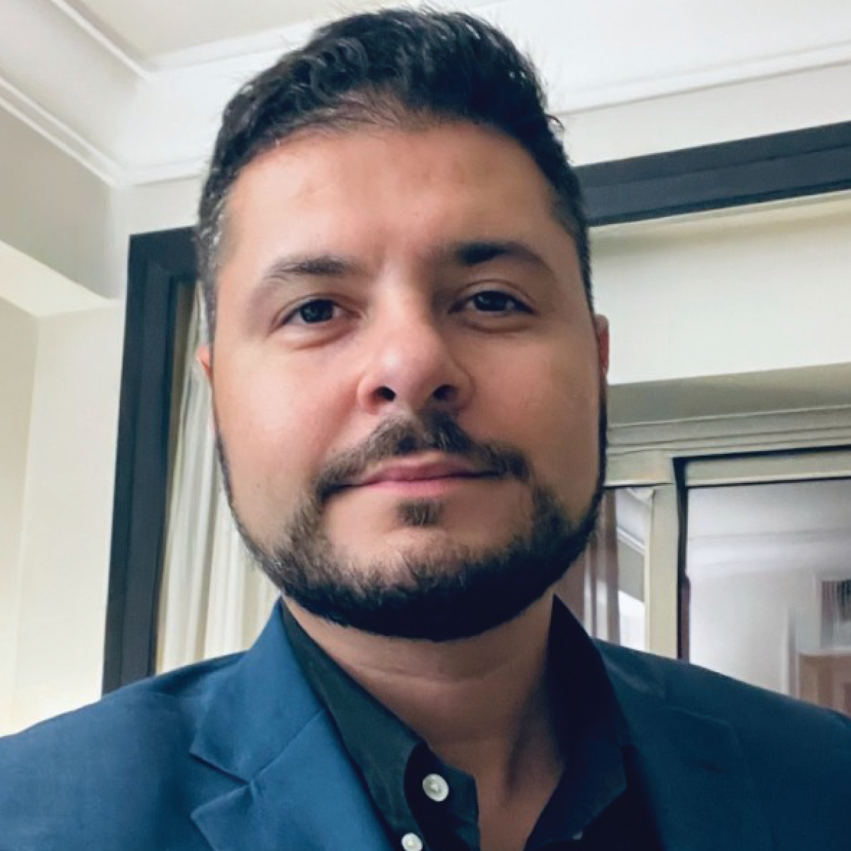 A man with a beard is wearing a blue suit and black shirt.