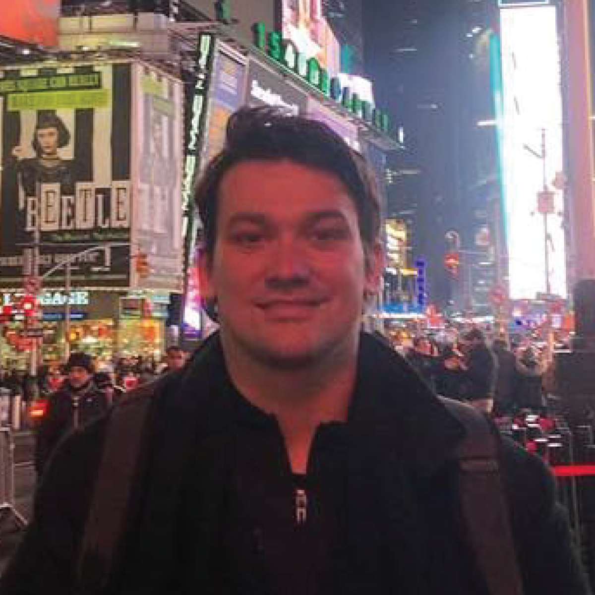 A man is standing in a crowded city street at night.