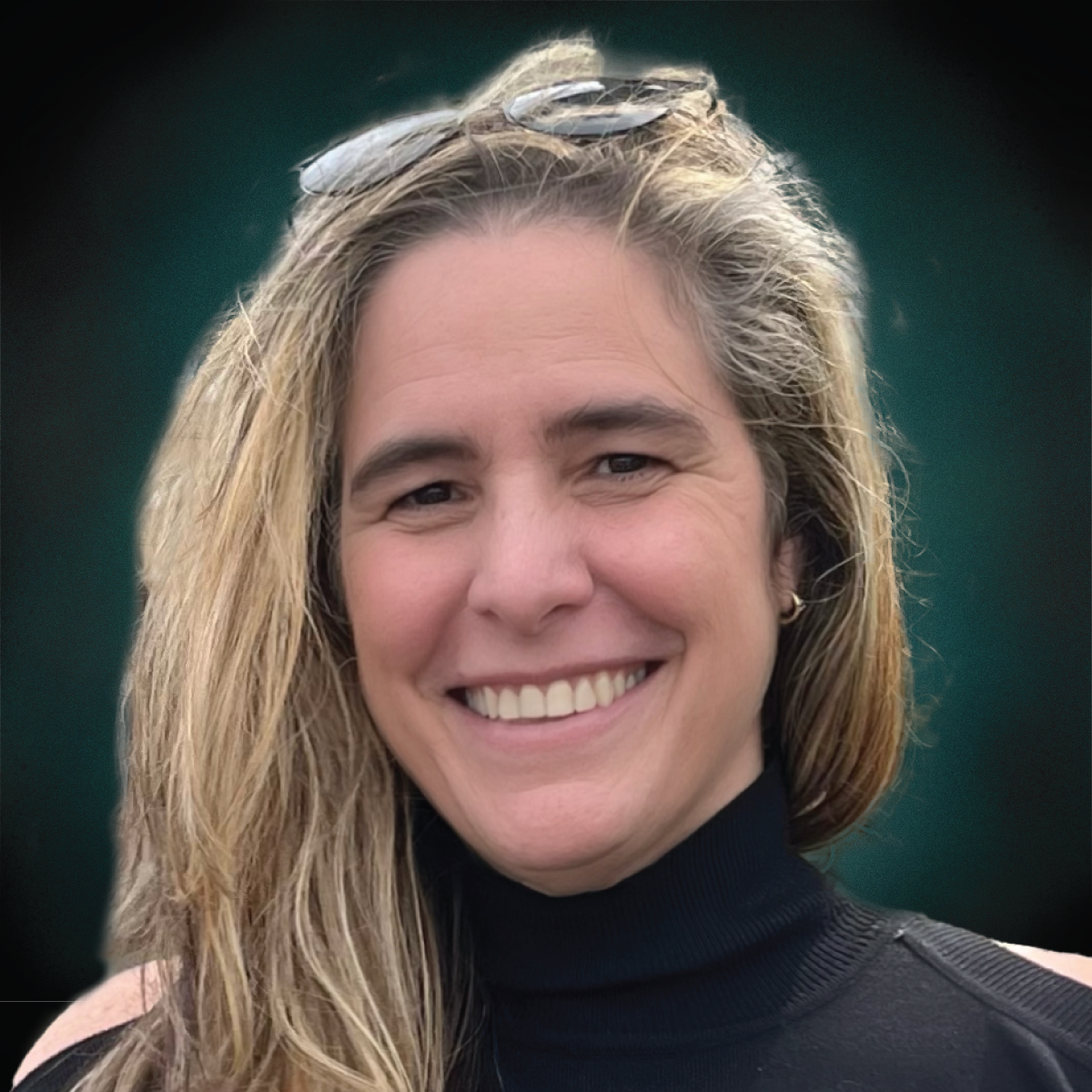 A woman wearing sunglasses and a black turtleneck smiles for the camera.