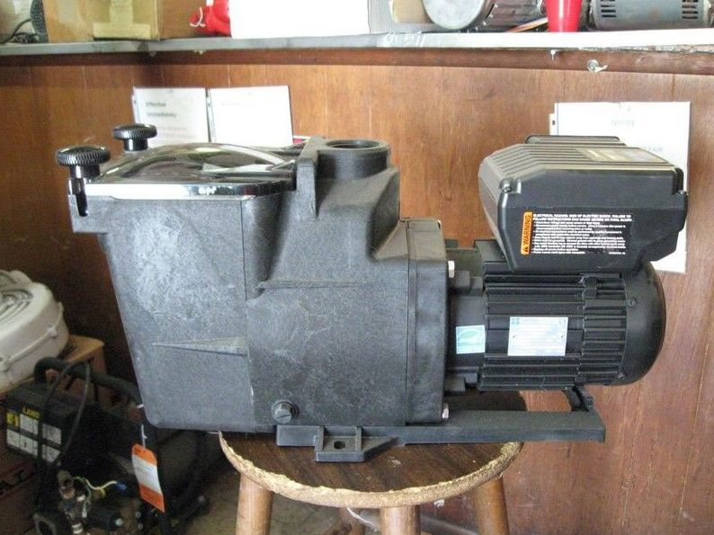 A black swimming pool pump is sitting on a wooden stool