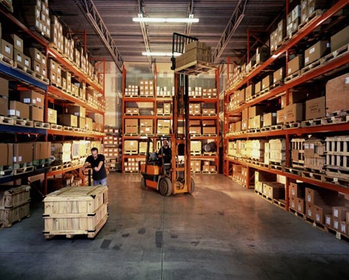 A man pushing a cart in a warehouse with a forklift