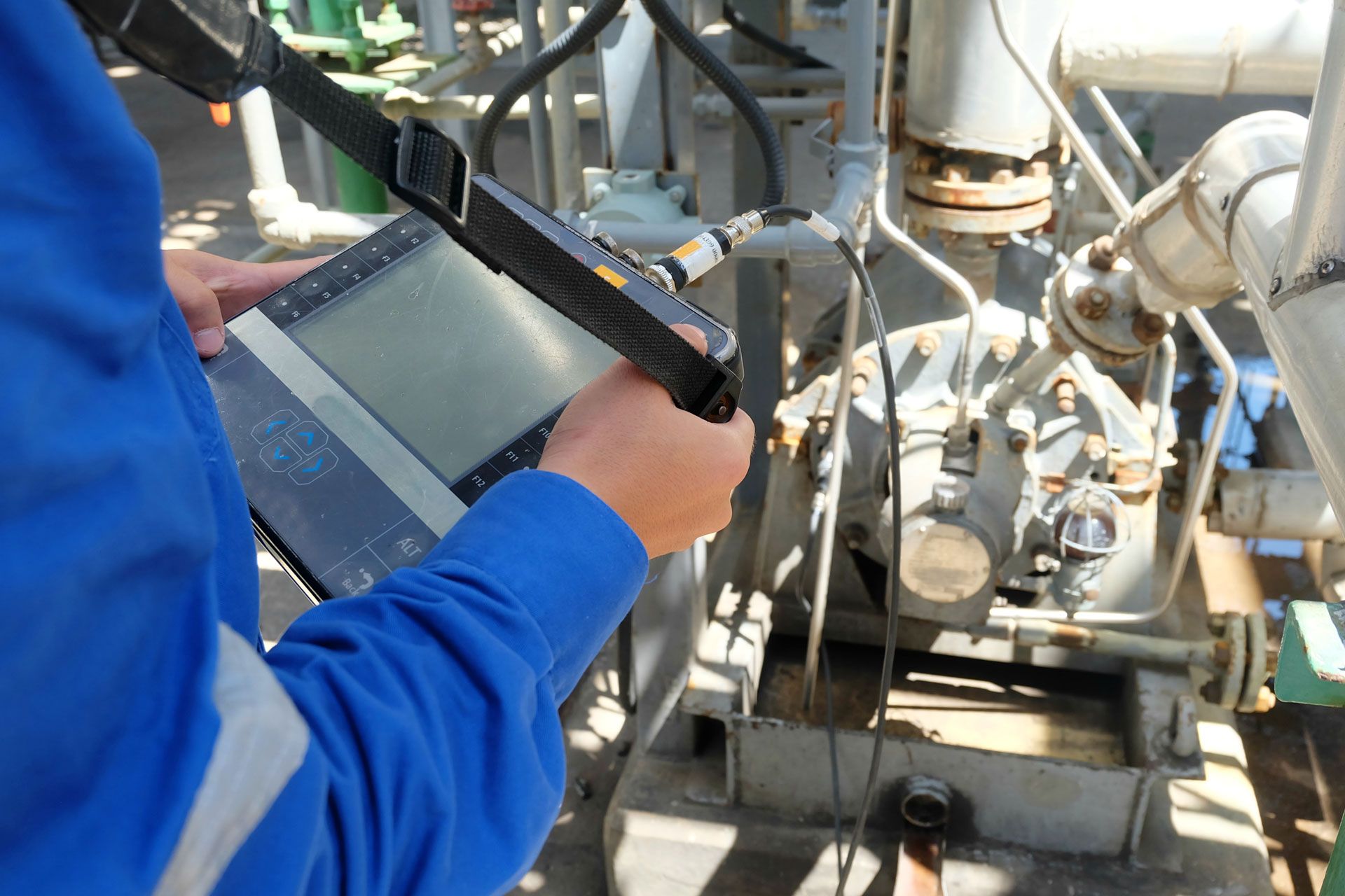 A man in a blue shirt is holding a tablet in front of a machine.