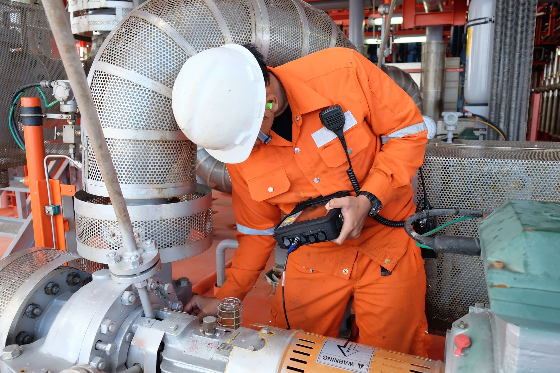 A man in an orange jumpsuit is working on a pipe in a factory.
