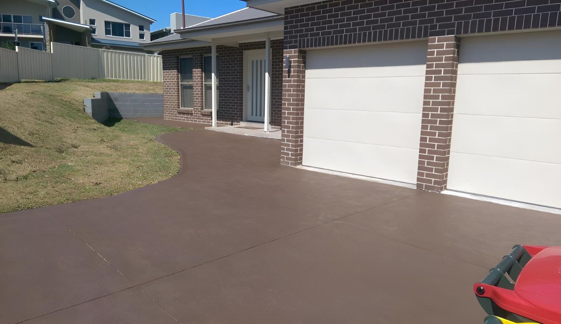 A Driveway Leading To A Brick House With Two Garage Doors — Concept Concreting NSW In Shellharbour, NSW