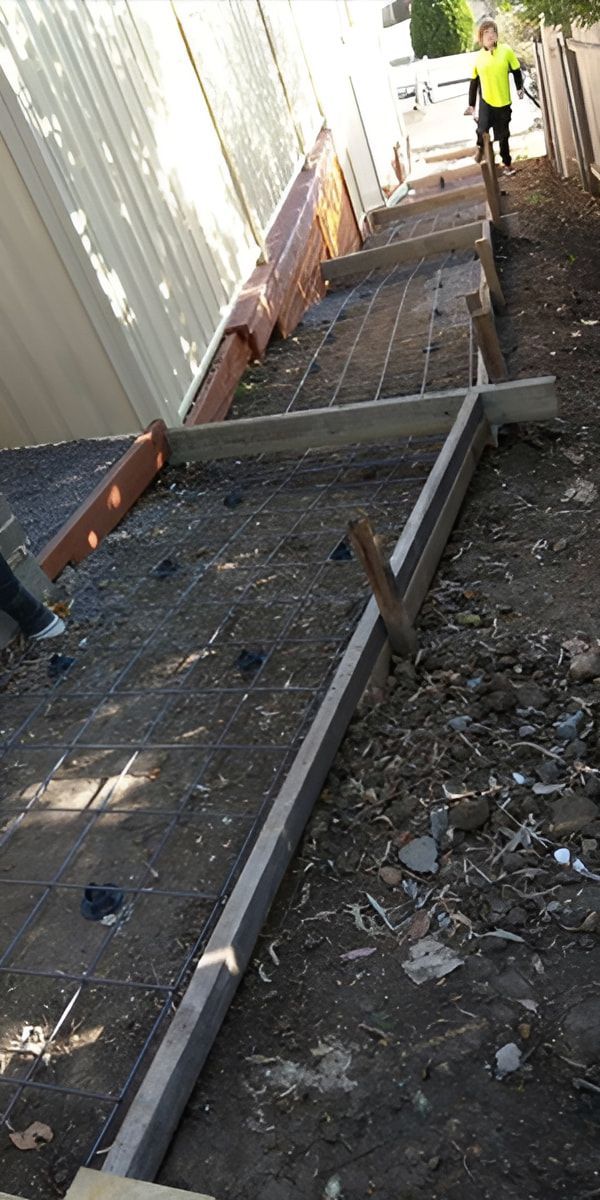 A Man Is Walking Down A Dirt Path Next To A Building — Concept Concreting NSW In Dapto, NSW