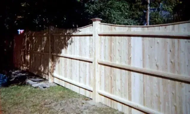 A wooden fence in a backyard with trees in the background.