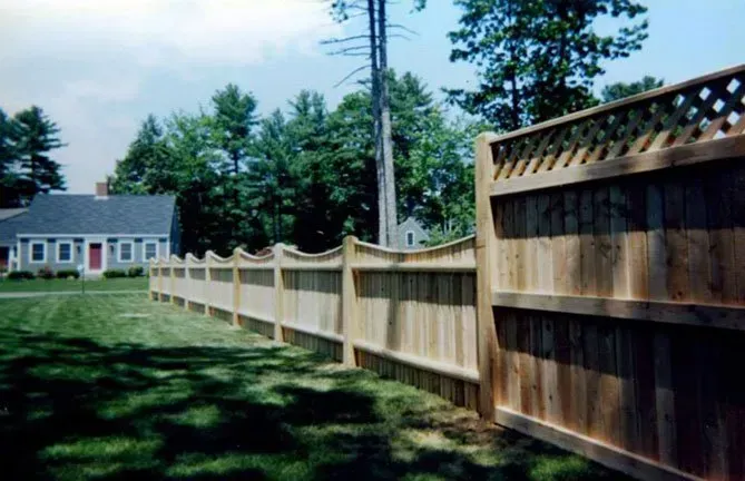 A wooden fence surrounds a lush green lawn in front of a house.