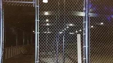 A chain link fence is surrounding a building at night.