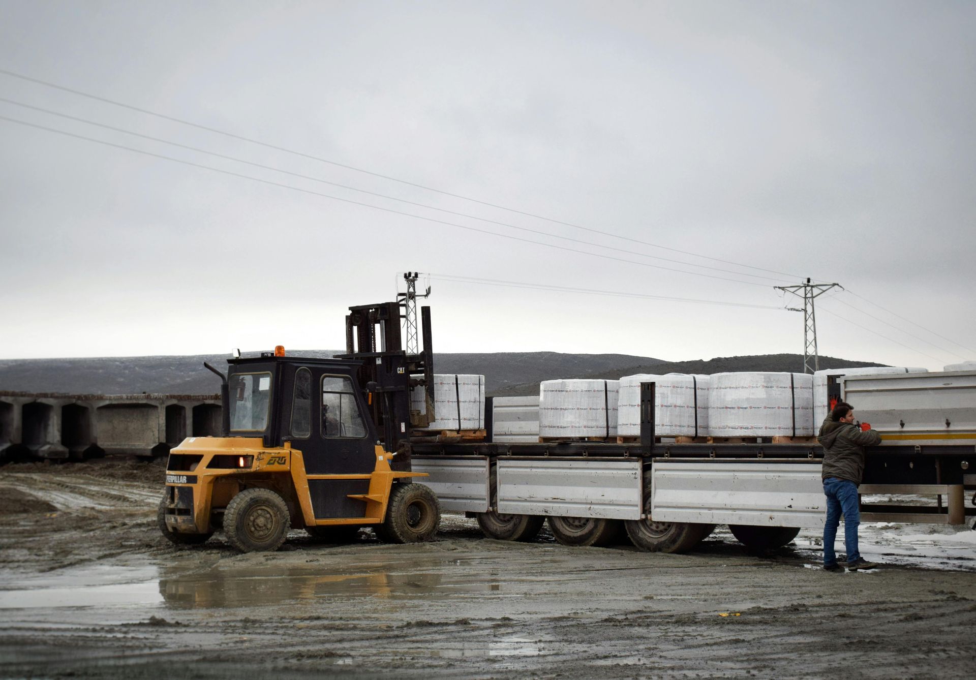A forklift is loading a truck with bricks in a muddy area.
