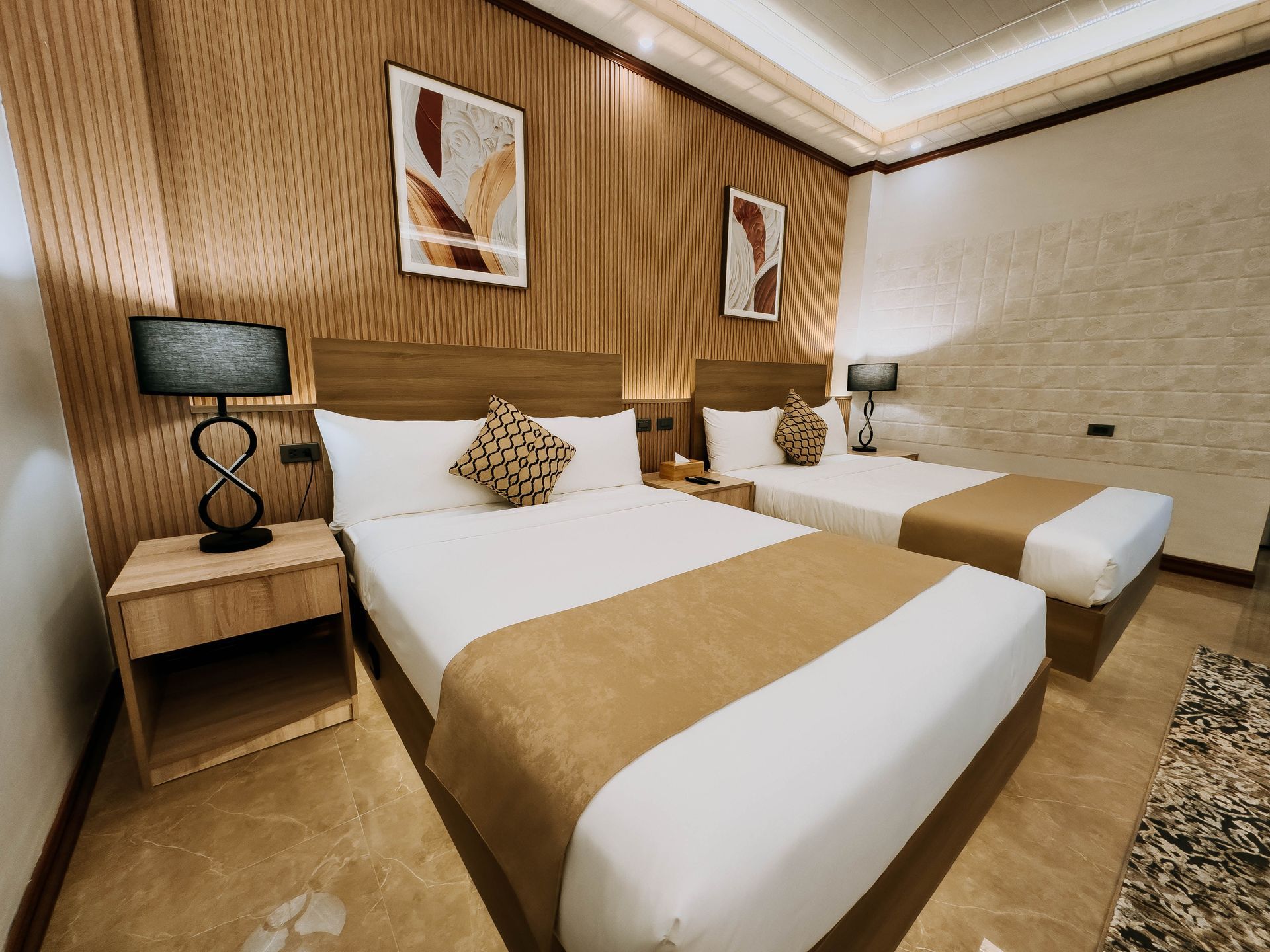 A hotel room with two beds, wooden headboard and walls, bedside tables, and abstract art.