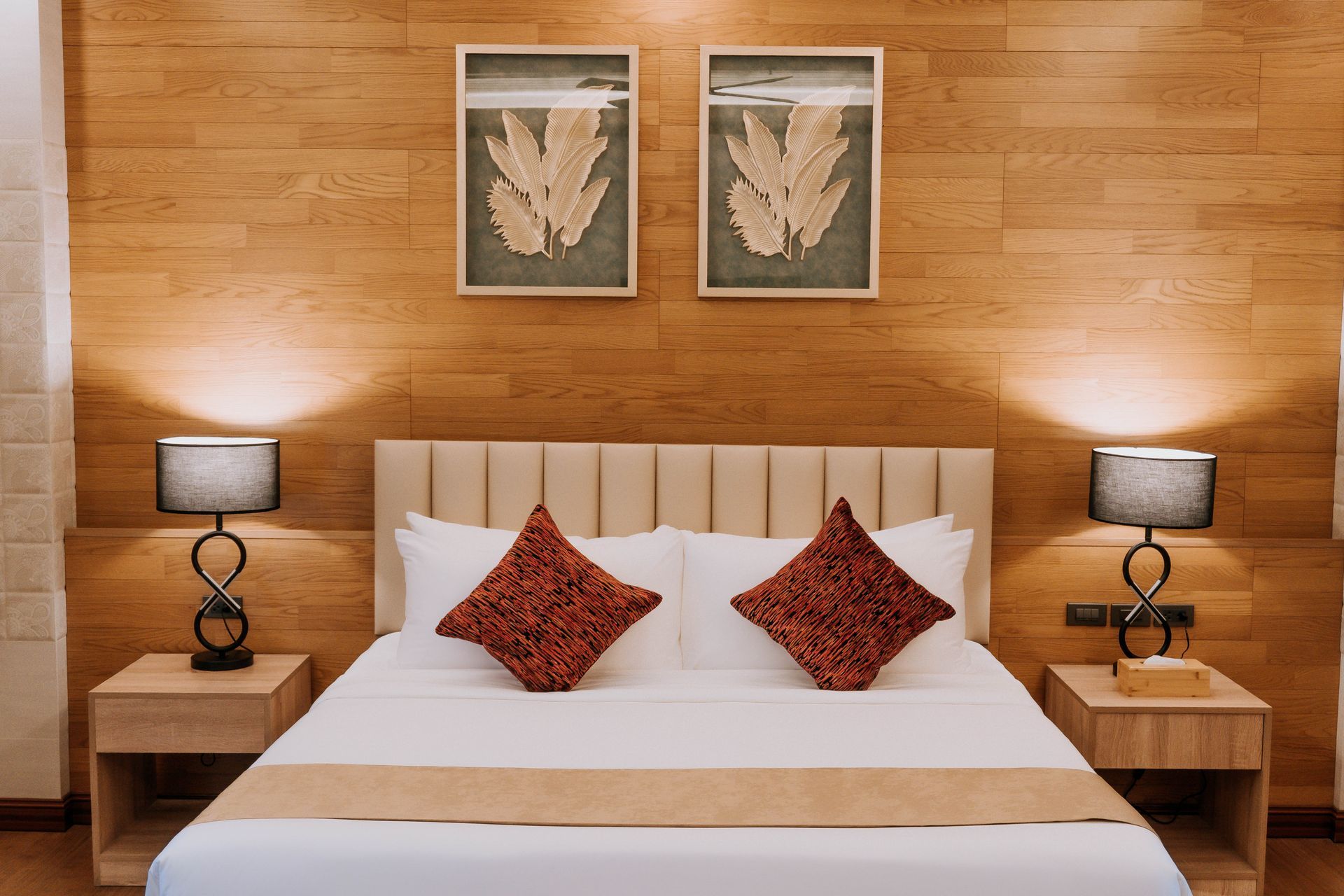 Bedroom with bed, nightstands, lamps, artwork, and wood paneling on the wall.