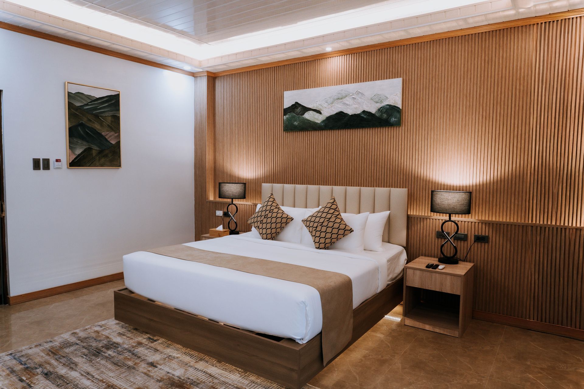 Bedroom with bed, art, wood paneling, lamps, nightstands, and rug.