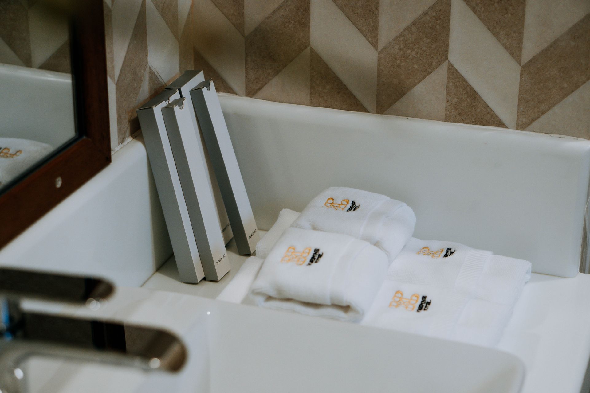 White sink with folded towels, toiletries, and a mirrored wall with patterned tiles.