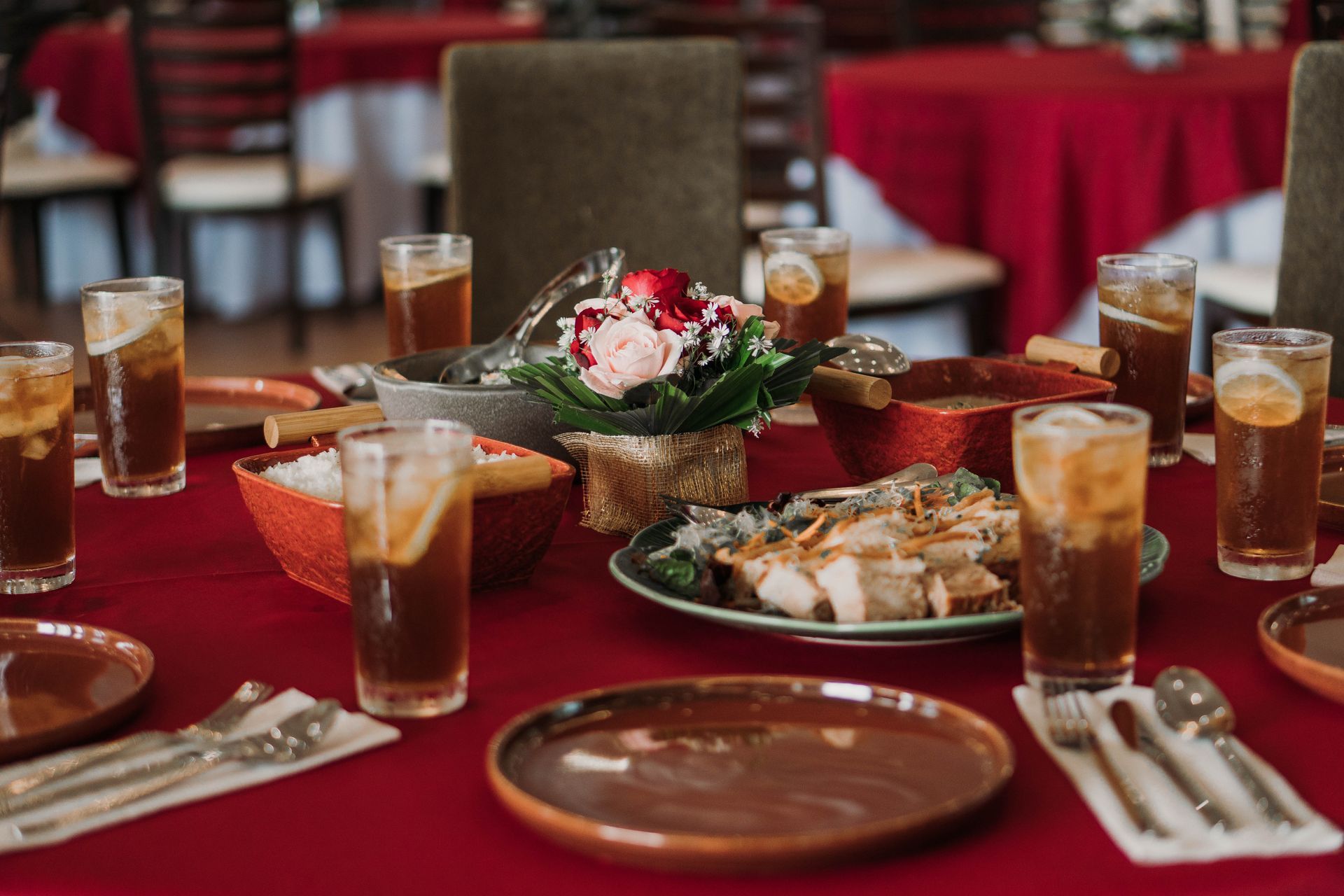 Festive table set with food, drinks, and flower arrangement on a red tablecloth.
