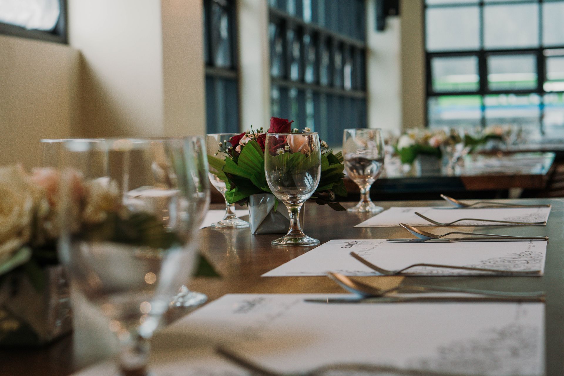 Restaurant table set with silverware, glasses, floral centerpieces, and place settings.