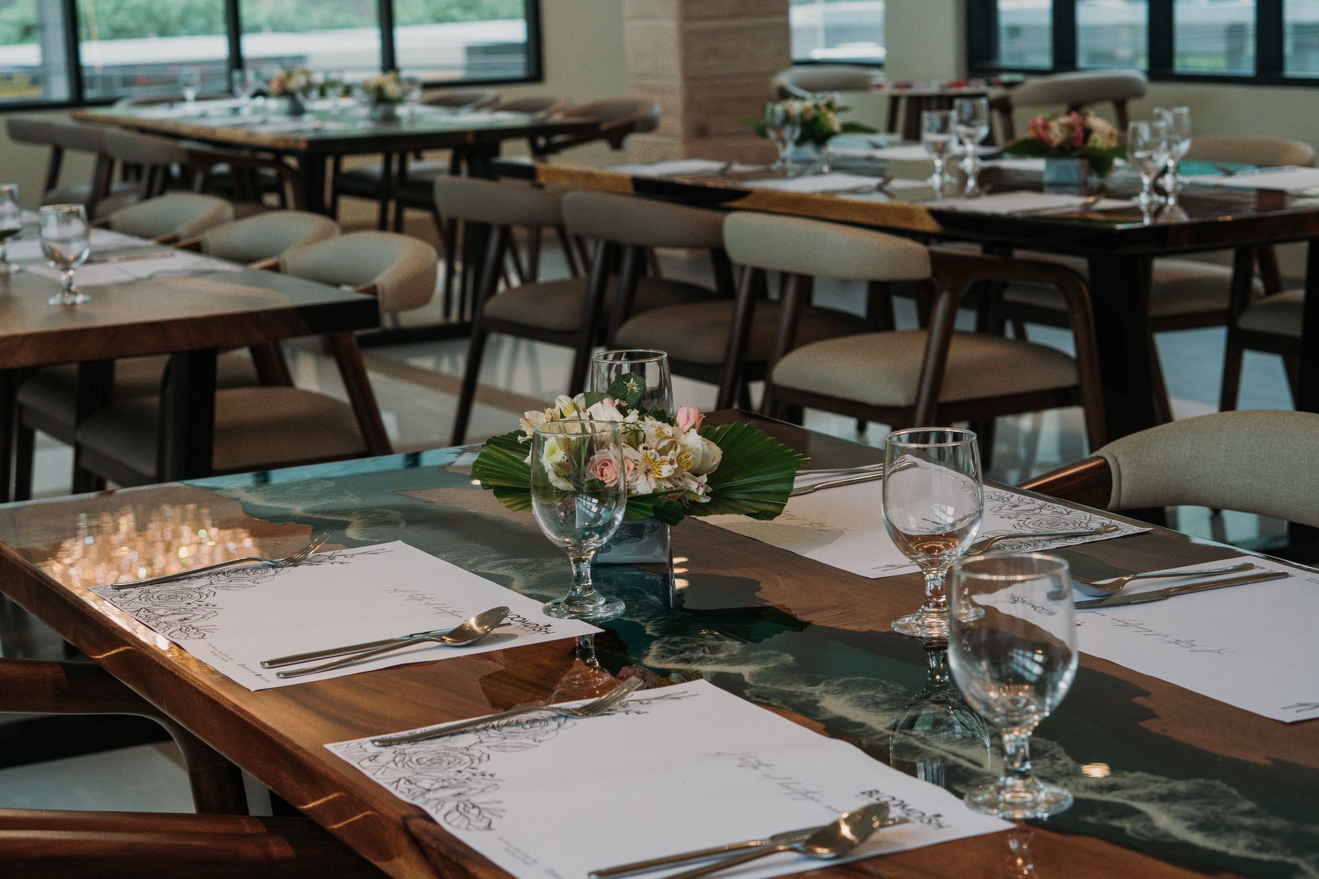 Restaurant dining room with wood tables, chairs, place settings, and floral centerpieces.