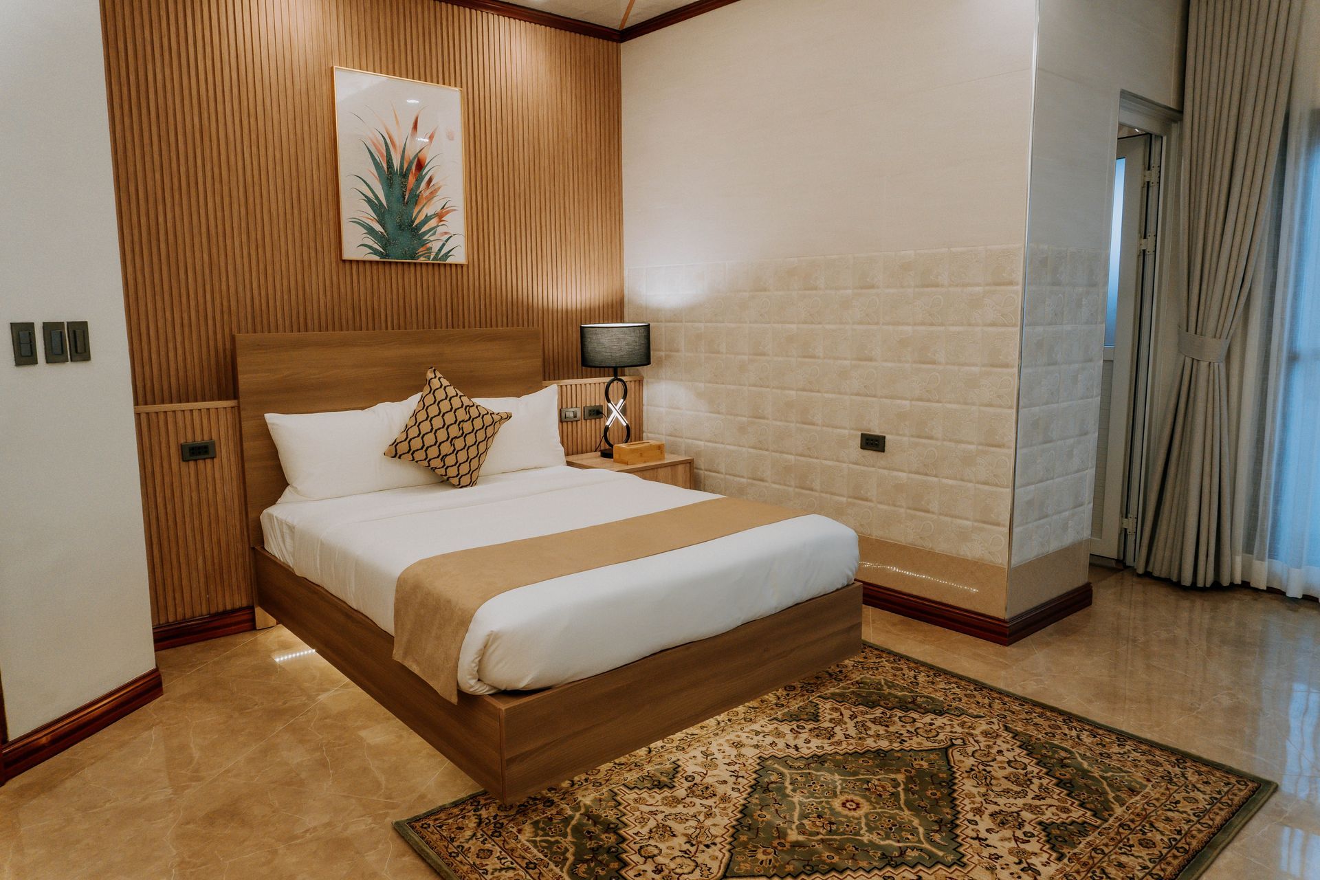 Bedroom with a bed, patterned rug, wood paneling, art, and a window with curtains.