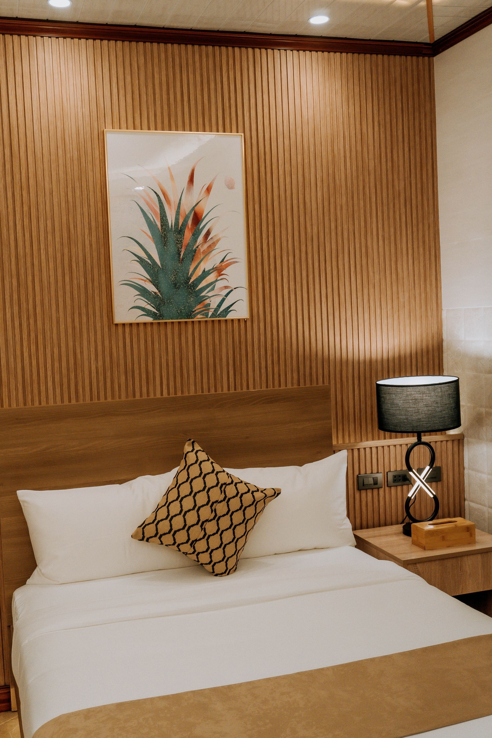 Bedroom with wooden headboard, a bed, and artwork on a textured wall. A lamp sits on a nightstand.