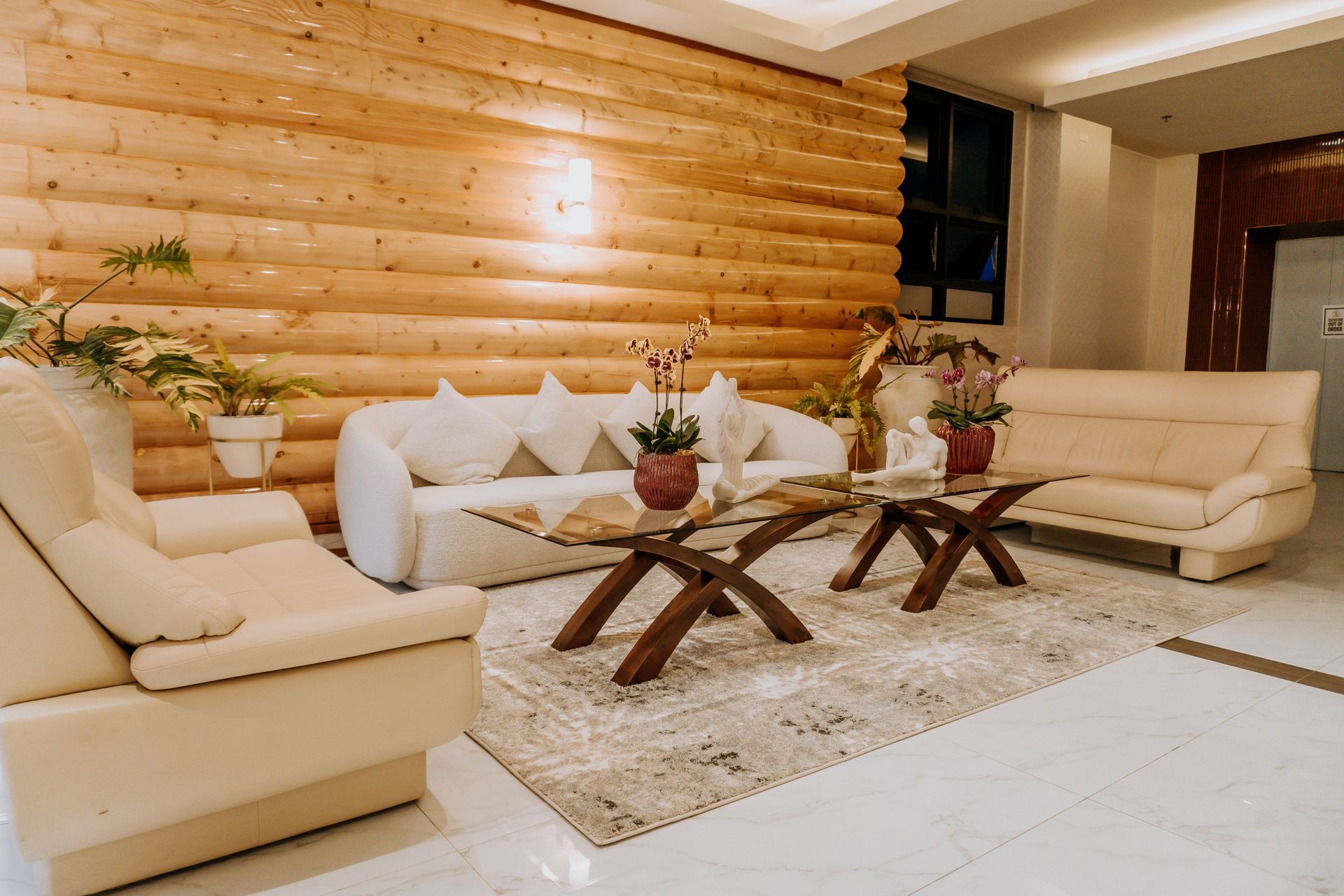 Lounge area with cream sofas, wooden accent wall, coffee tables, and plants on a beige rug.