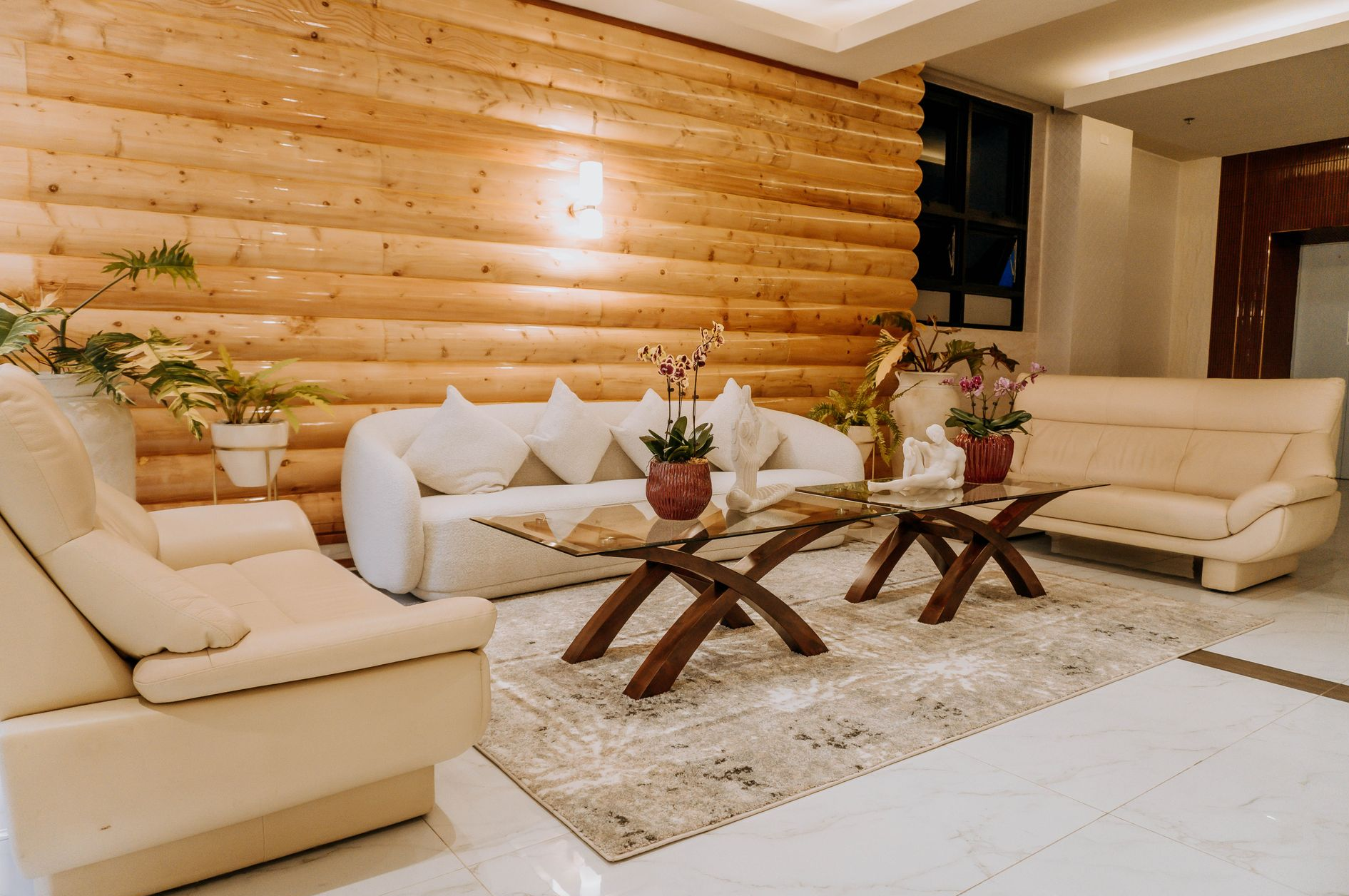 Lounge area with cream sofas, wooden accent wall, coffee tables, and plants on a beige rug.