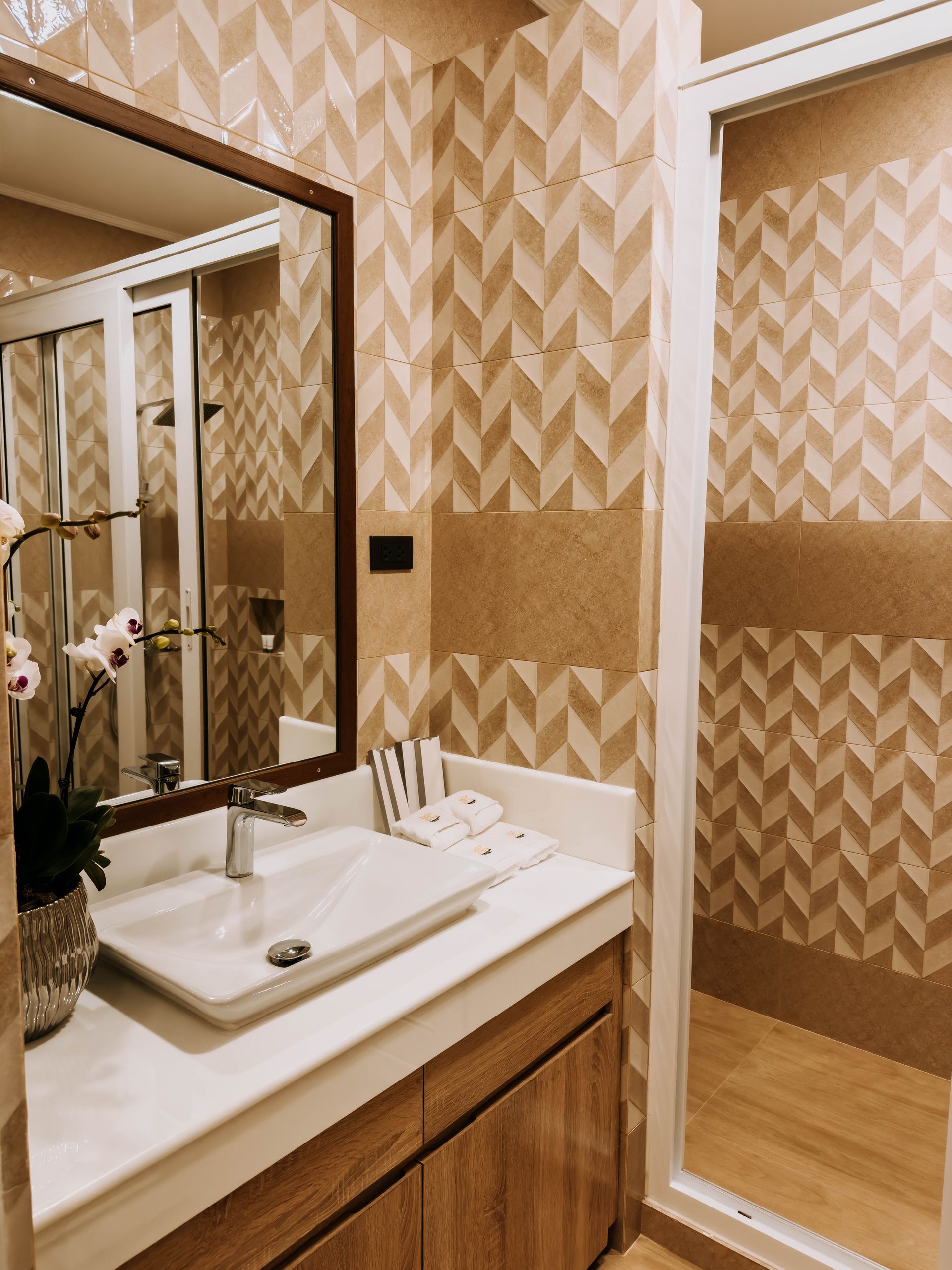 Bathroom with patterned beige walls, white sink, and glass shower door.