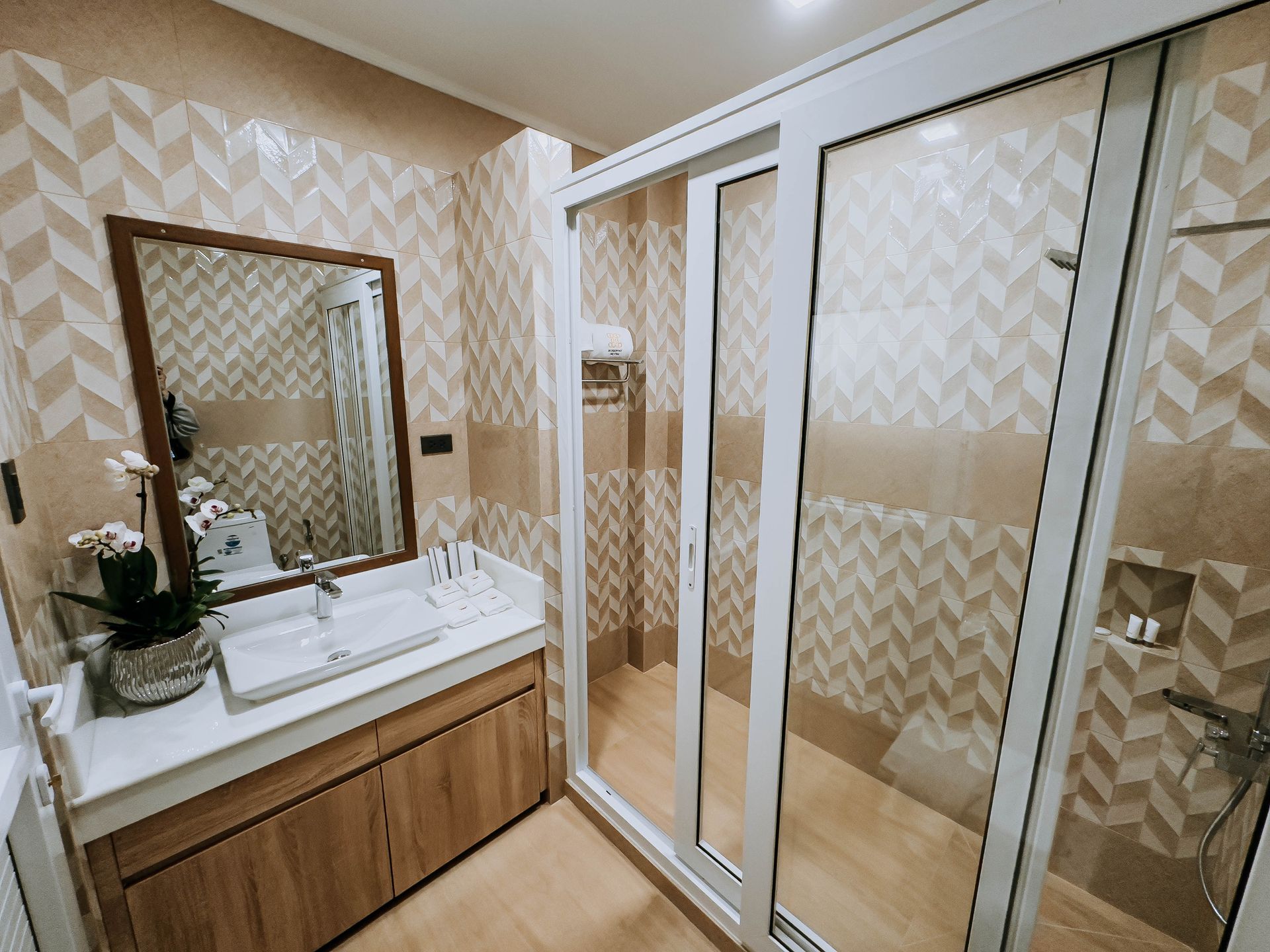 Bathroom with glass shower, wooden vanity, and patterned tile walls.