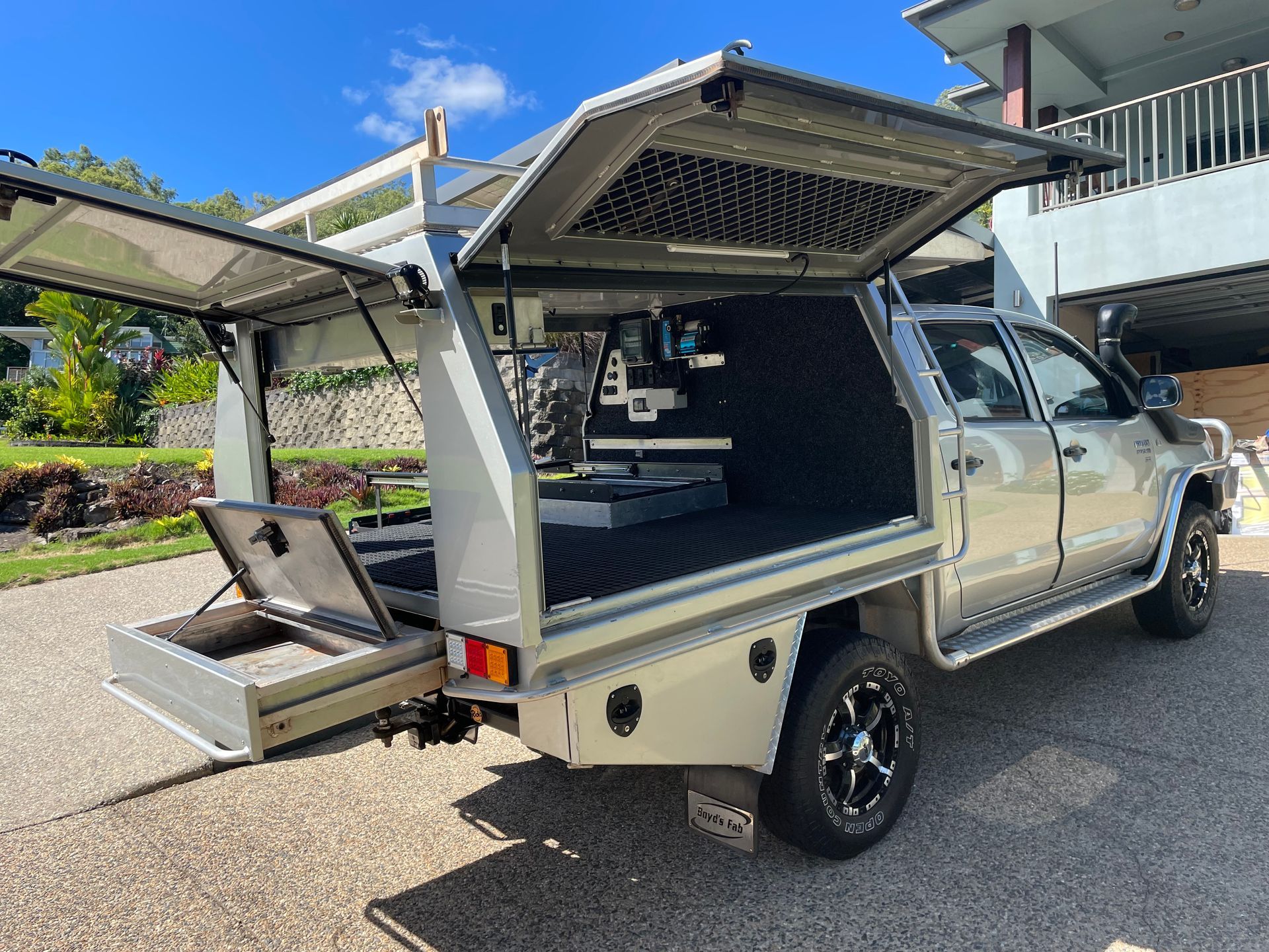 Silver work truck with open storage compartments in a residential driveway.— Boyd's Fabrications In Portsmith, QLD 