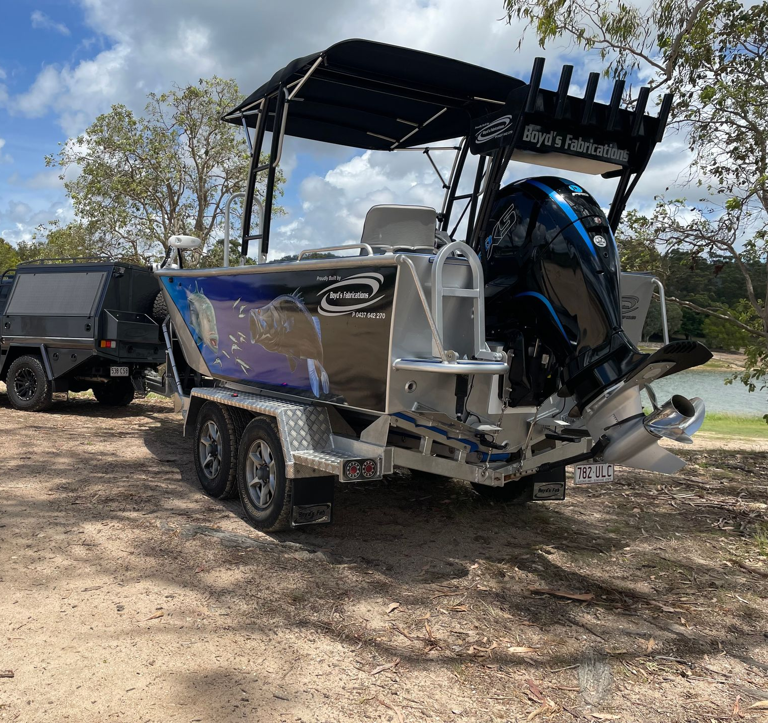 Boat with canopy and a black trailer, parked on a grassy bank.— Boyd's Fabrications In Portsmith, QLD 