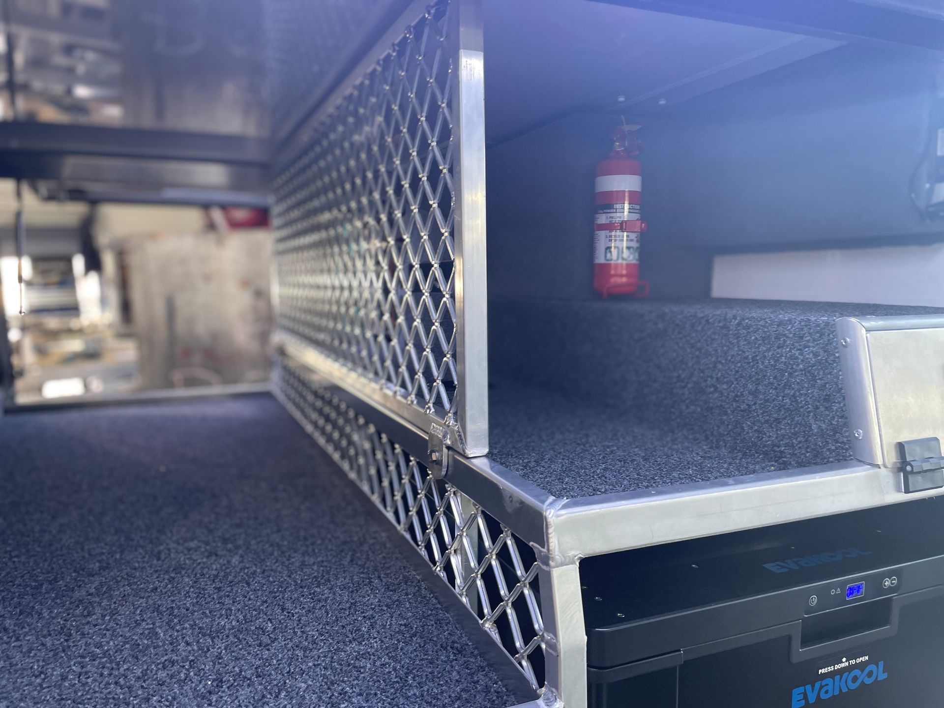 A metal storage compartment with a mesh door, a fire extinguisher, and a cooler.— Boyd's Fabrications In Portsmith, QLD 