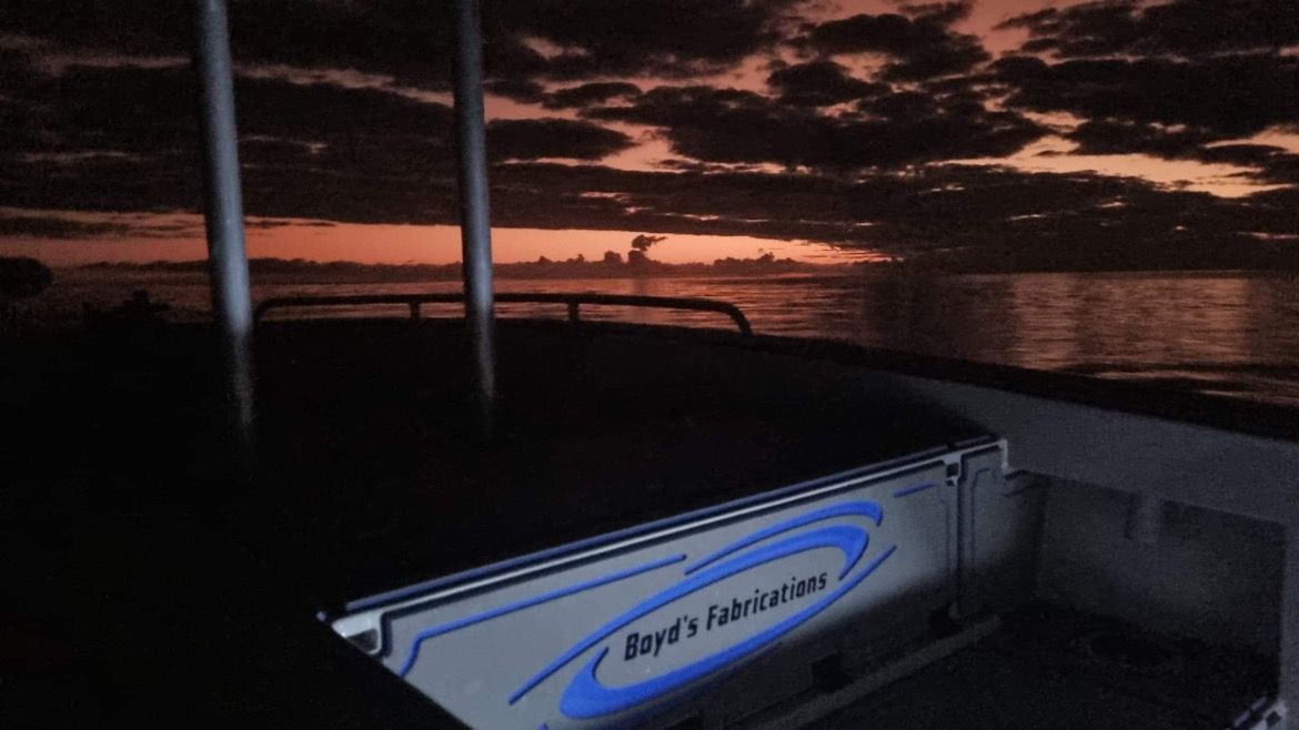 Boat deck at dusk, silhouetted against a colorful sunset sky, with 