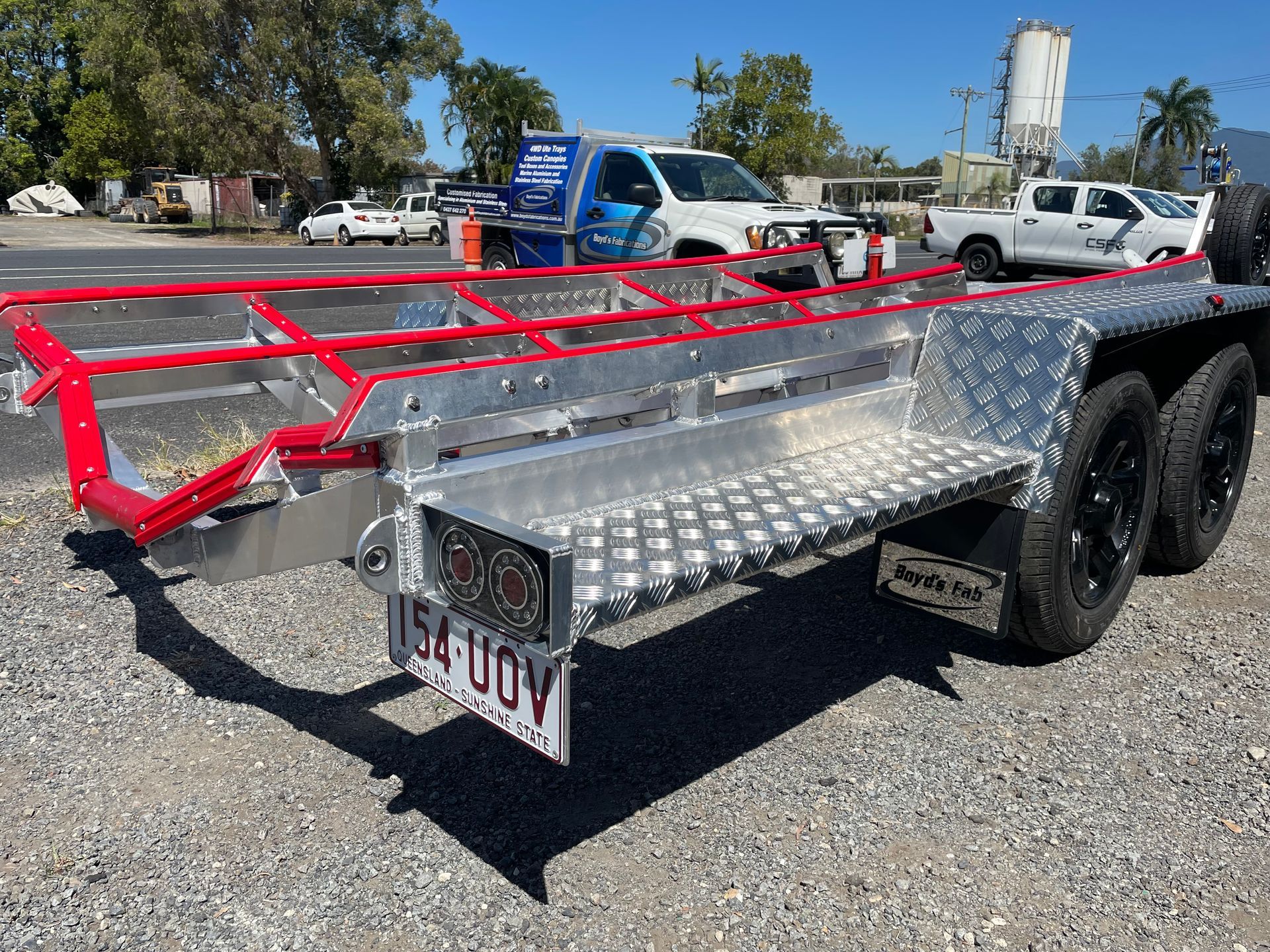 Diamond-plated trailer with red side rails, black wheels, license plate, outdoors, sunny day.— Boyd's Fabrications In Portsmith, QLD 