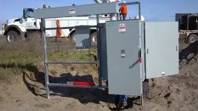 A large electrical box is sitting in the dirt next to a truck.