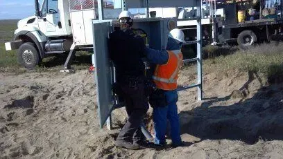 Two men are working on a box in the dirt in front of a truck.