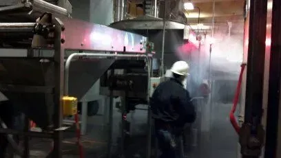 A man in a hard hat is standing in a room with smoke coming out of it.