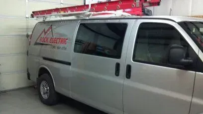 A silver van is parked in a garage with a ladder on top of it.
