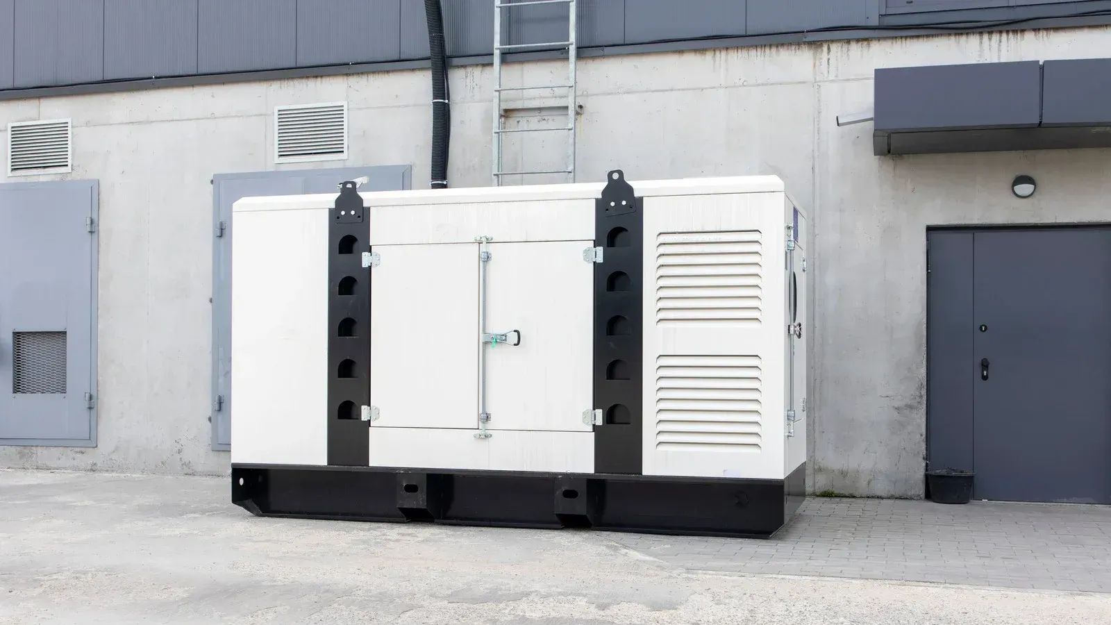 A large, white industrial generator sits outside a grey concrete building next to a door.