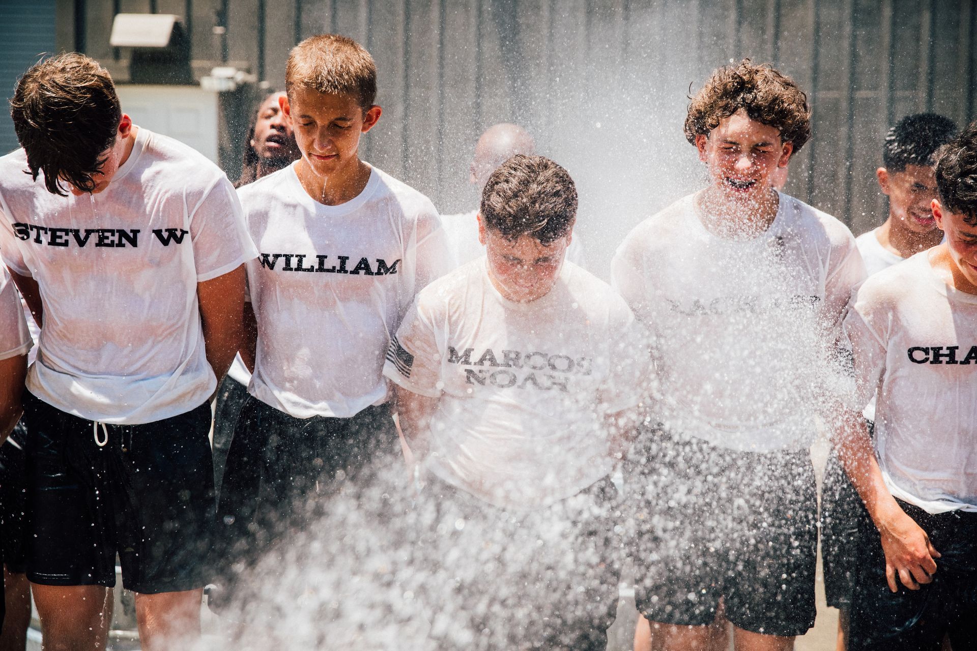 A group of young men are standing in front of a wall covered in water.