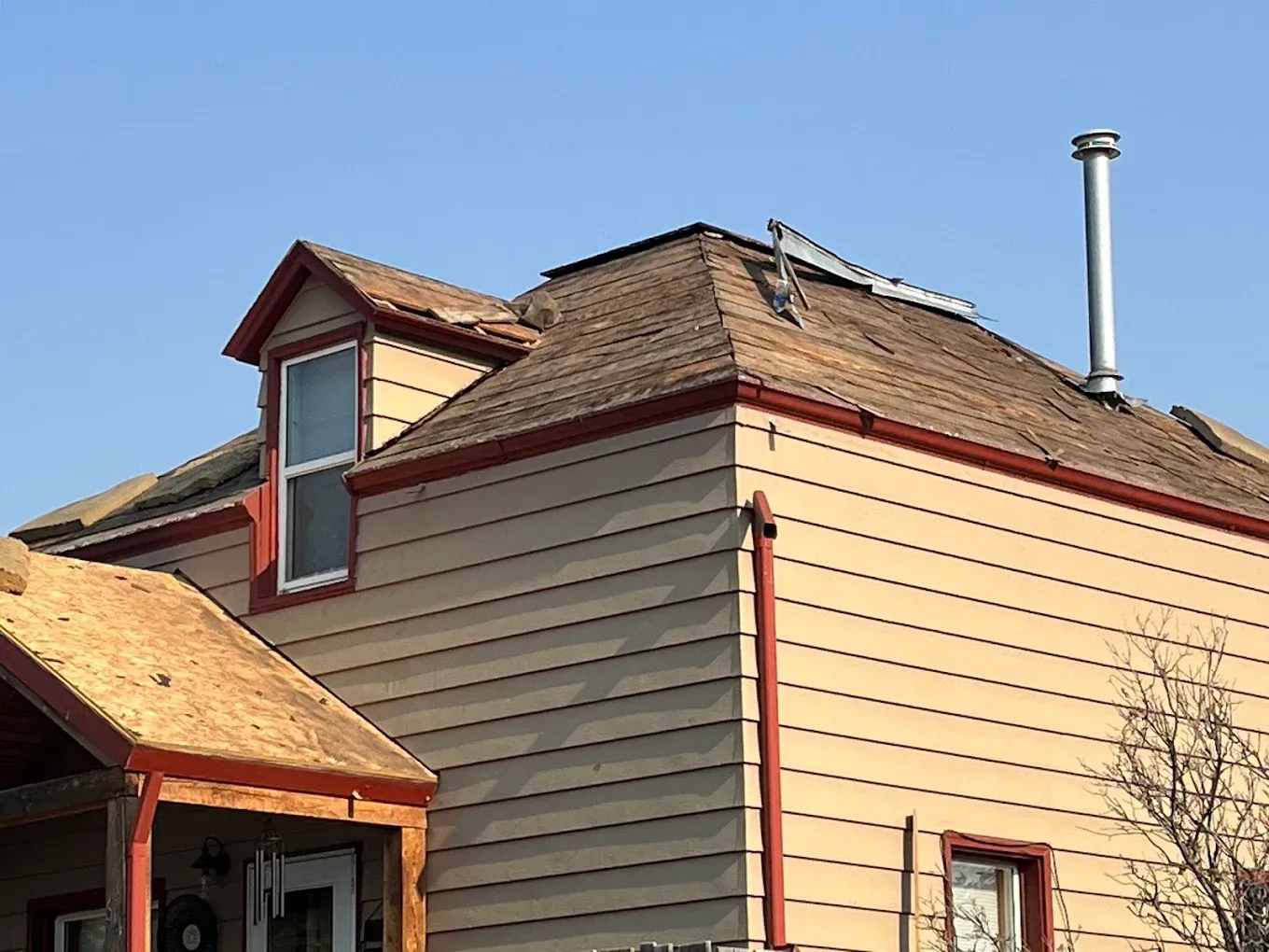 Tan house with brown roof, red trim, dormer, chimney, and blue sky.